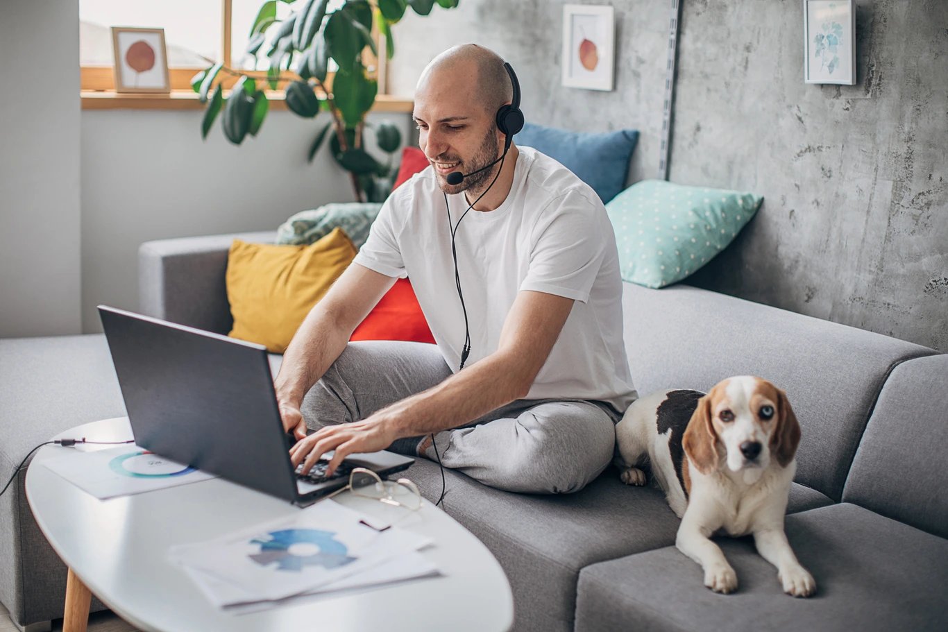 man-on-couch-sitting-at-laptop-on-headset-with-dog