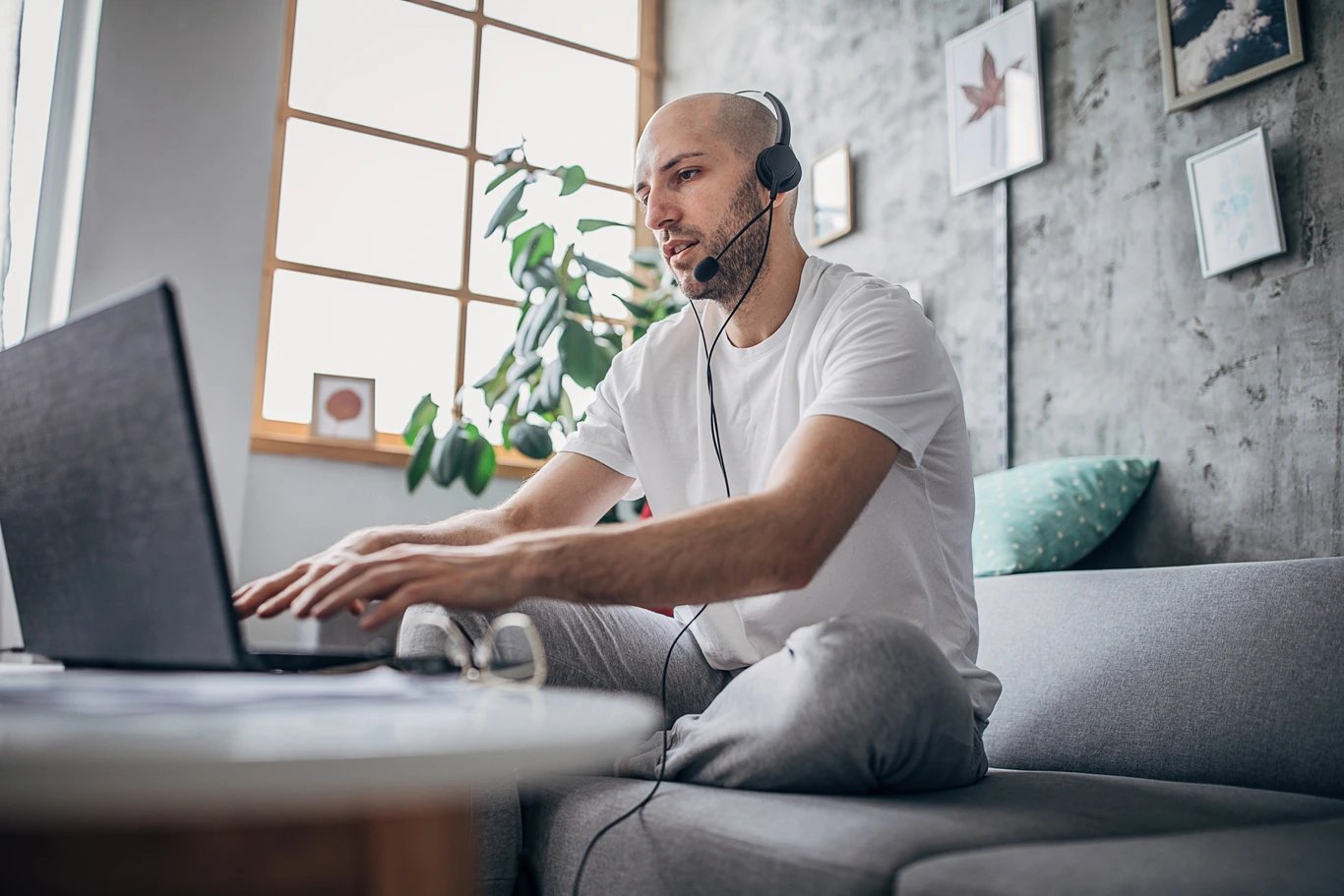 man-on-couch-typing-on-laptop-with-headset