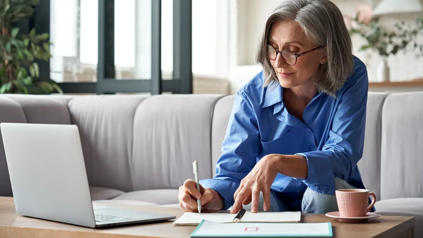 woman working on laptop writing notes on paper